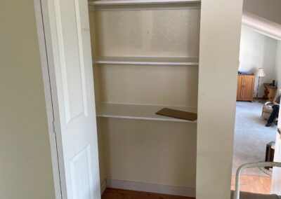 Open white bi-fold closet doors revealing interior shelves of a newly built linen closet in a hallway renovation.