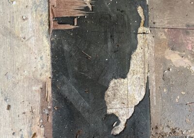 Close-up of a damaged subfloor with worn-out layers of plywood and old black underlayment.