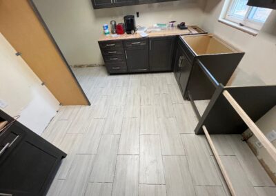 Freshly installed light gray tile flooring in a kitchen remodel, complementing dark cabinetry.