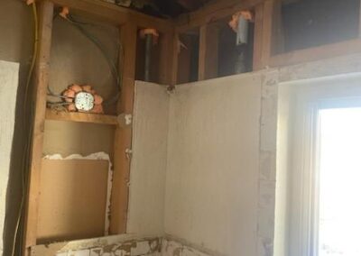 Partially demolished wall in a kitchen renovation, exposing wooden framing, electrical wiring, and old plaster.