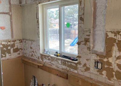 Kitchen wall stripped down to expose plumbing, electrical wiring, and insulation upgrades.