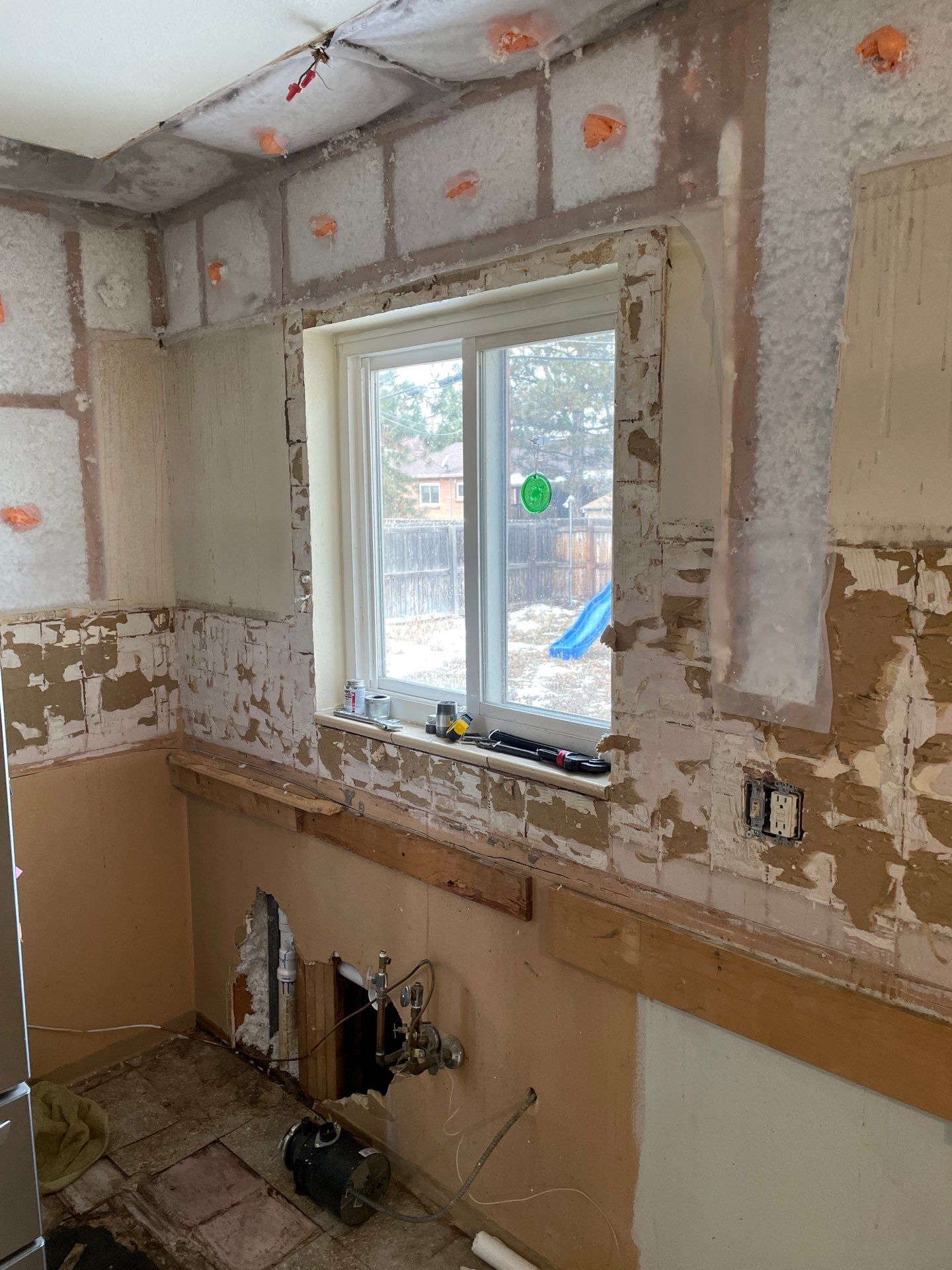 Kitchen wall stripped down to expose plumbing, electrical wiring, and insulation upgrades.