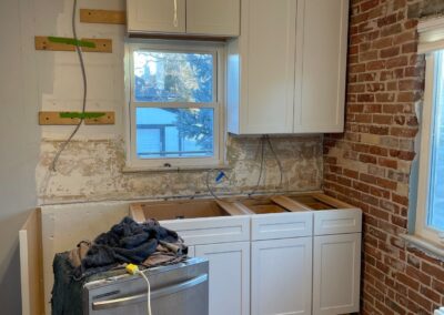 New white shaker cabinets partially installed using a French cleat mounting system against a brick kitchen wall.