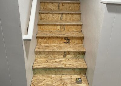 Basement stairs mid-repair, showing newly installed OSB treads replacing damaged original