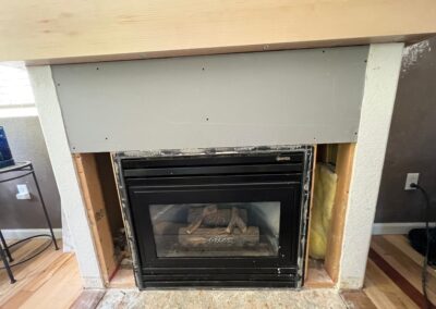 Fireplace surround partially opened, exposing insulation and wall framing with the new mantel installed.