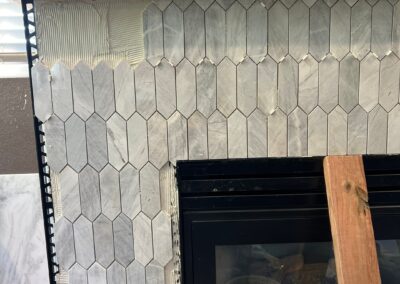 Close-up of marble picket tile partially installed on fireplace surround with thinset applied.