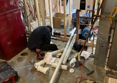 Technician installs new PVC plumbing lines in a basement renovation project surrounded by tools, piping, and insulation.