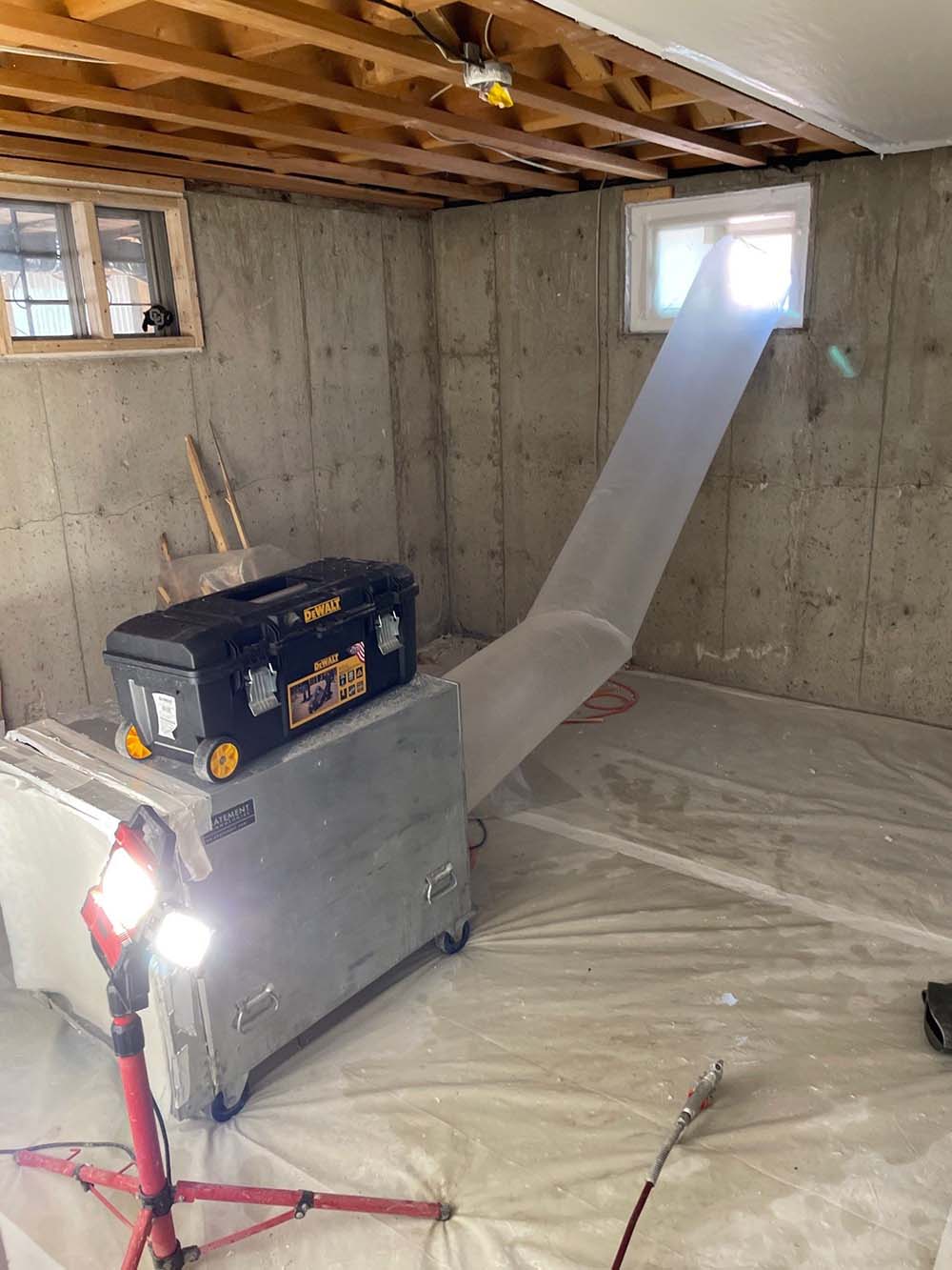 Contractor dismantling a dropped ceiling in a blue room with exposed insulation and hanging fluorescent light.